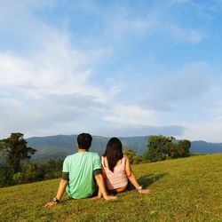 Rear view of friends sitting on field against sky