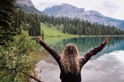 Rear view of woman with arms raised looking at lake against mountain