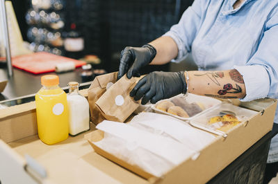 Midsection of female chef keeping take out meal packs in cardboard box at restaurant kitchen counter during coronavirus