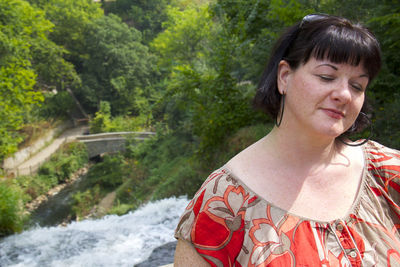 Overweight woman with eyes closed against waterfall