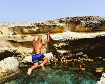 Rear view full length of man jumping into sea against rock formation