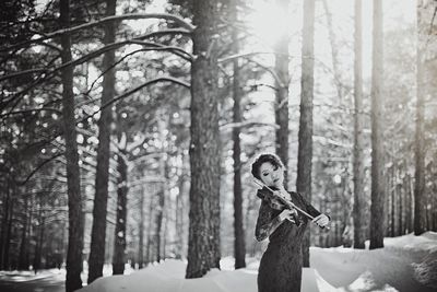 Woman playing violin in forest during winter