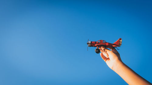 Low angle view of hand holding toy airplane against clear blue sky