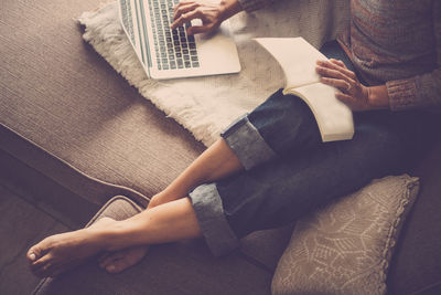 Low section of woman using laptop on sofa at home