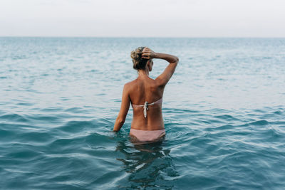 View from the back of a woman standing in the sea and ready to swim.