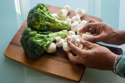 Cropped image of person holding vegetables on cutting board