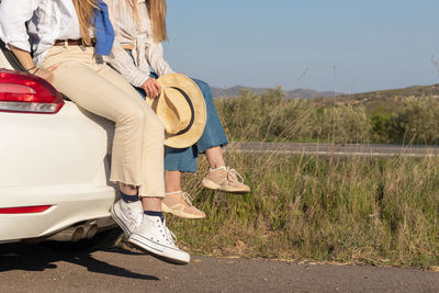 Legs of two unrecognizable girl friends sitting in the car truck of the white car admiring sunset