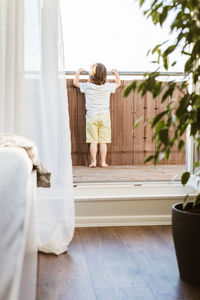 A little boy stands on a balcony at home or in a hotel room and looks into the distance. expectation