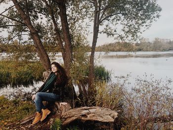 Portrait of young woman sitting by lake against trees