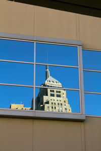 Low angle view of building against blue sky reflected in window