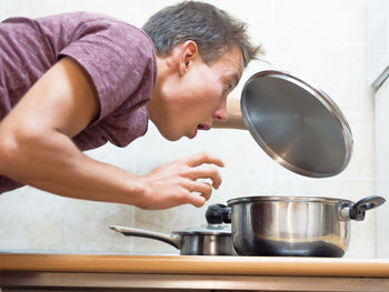 Side view of surprised young man looking at cooking pan on table