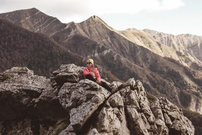 Man on rocks by mountains against sky