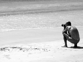 Full length of shirtless man photographing at beach