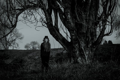 Spooky man in costume standing by majestic tree on grassy field