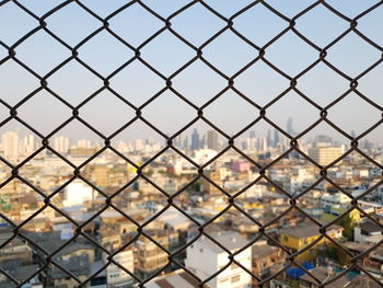 Close-up of chainlink fence against cityscape