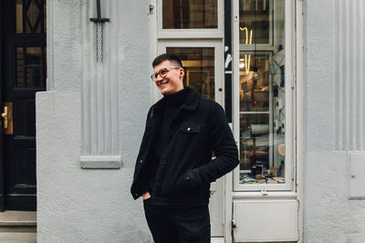 Smiling young man looking away while standing against store