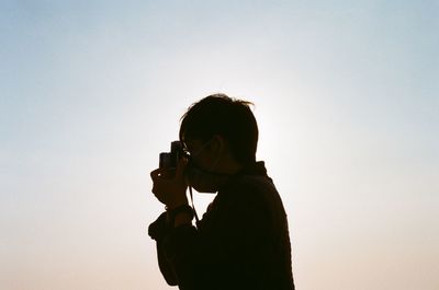 Silhouette man photographing against sky during sunset