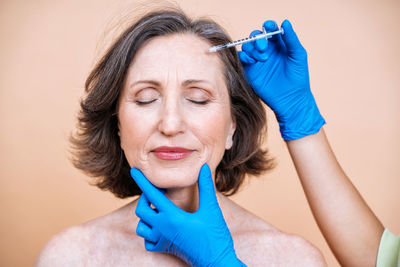 Cropped hand of beautician treating patient against colored background