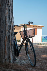 Bicycle parked by tree trunk against clear sky