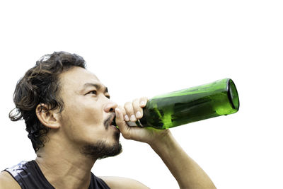 Portrait of young man drinking beer bottle against white background