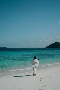 Rear view of woman walking at beach against sky
