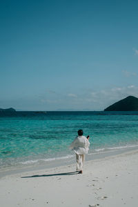 Rear view of woman walking at beach against sky