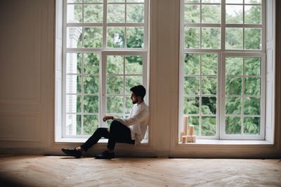 Man sitting on window sill at home