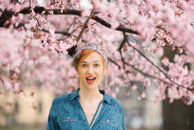 Portrait of happy young woman with pink cherry blossoms against trees