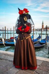 Woman wearing costume and mask against gondolas during venice carnival