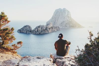 Rear view of man sitting on rock against sky