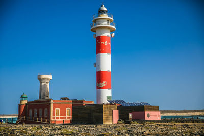 Lighthouse by building against clear blue sky