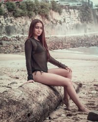 Side view portrait of seductive woman sitting on driftwood at beach