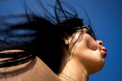 Low angle view of young woman puckering lips against clear blue sky during sunny day