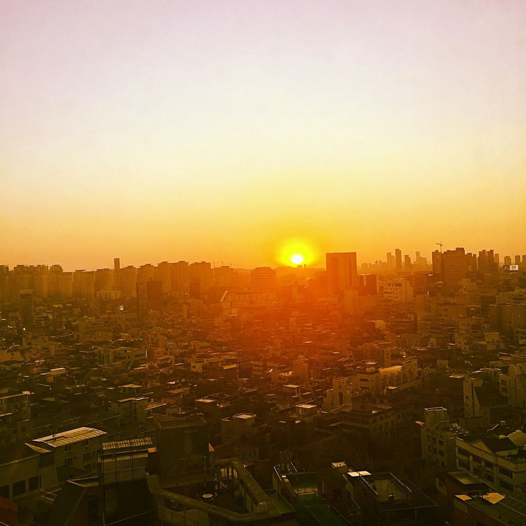 sunset, building exterior, cityscape, city, architecture, built structure, sun, orange color, crowded, high angle view, skyscraper, residential district, copy space, sunlight, clear sky, residential building, sky, city life, residential structure, urban skyline