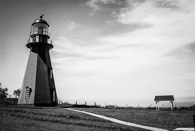 Lighthouse on field against cloudy sky