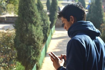 Side view of man using mobile phone while standing by plants