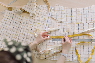 High angle view of woman measuring fabric with tape and ruler on table