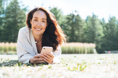 Adult curly hair smiling woman in casual using mobile phone in city park