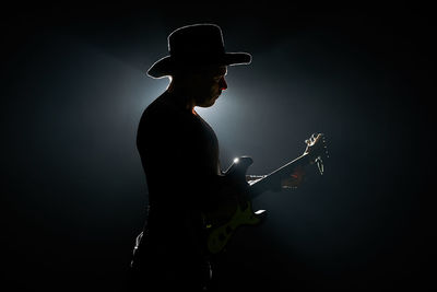 Side view of silhouette mid adult man playing guitar against black background