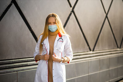 Portrait of doctor wearing mask standing against building