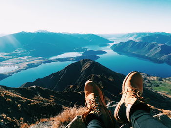 Low section of man relaxing on mountain against sky