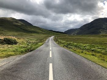 Road leading towards mountains against cloudy sky