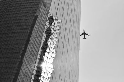 Low angle view of modern building against silhouette airplane flying in clear sky