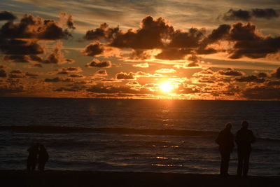 Silhouette people at beach against sky during sunset