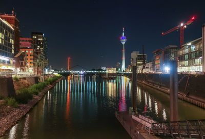 Illuminated bridge over river by buildings against sky at night