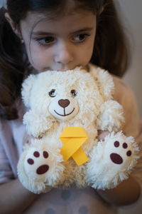 The girl holds in her hands a toy teddy bear with a yellow ribbon.