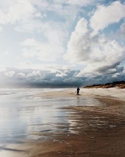 Distant view of person at beach against cloudy sky