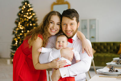 Happy young parents with their baby in their arms in the living room celebrate christmas