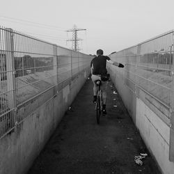 Rear view of man riding bicycle on footbridge