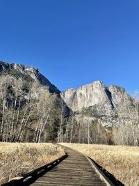 Footpath by mountain against clear blue sky